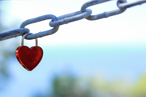 Love locks and hearts. Close-up of love lock with a red heart hanging on chain in on background of the sea. The key locks for lovers promise love. Concept image for valentine's day. Loyalty