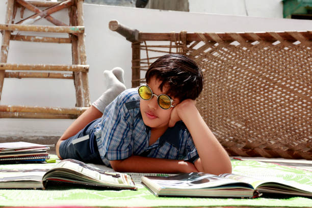 School boy of Indian ethnicity lying down on the floor at home and reading his text book portrait close up at home wearing school uniform.