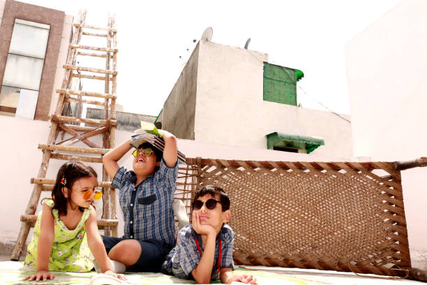 Elementary age brother and his cute little sister lying down on the floor near ladder at home wearing school uniform reading text book together portrait close up at home. One boy carrying stack of text book on the head in background,