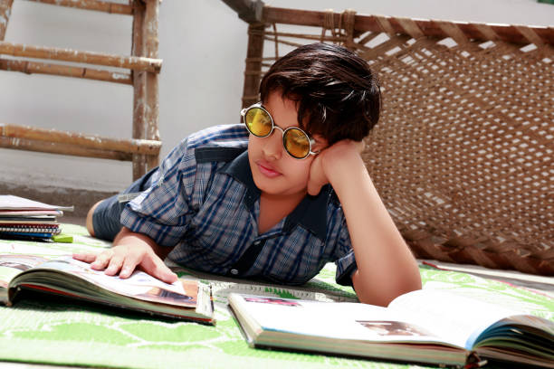 School boy of Indian ethnicity lying down on the floor at home and reading his text book portrait close up at home wearing school uniform.