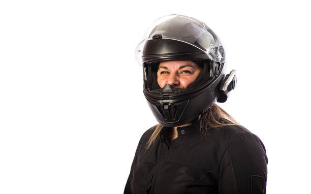 Curly haired Caucasian young man sitting on his motorcycle using mobile phone smiling, with direct sunlight and grass in the background. Lifestyle concept