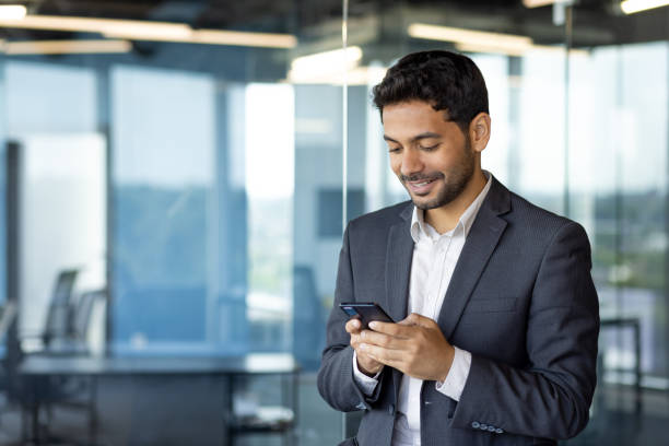 istock Young arab businessman holding phone, man inside office at workplace typing message and browsing online sites, worker using app on smartphone 1598828850