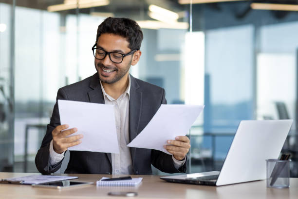istock Successful mature experienced financier on paper work, Arab smiling satisfied with results of financial achievement, reviewing contracts, invoices and statements with accounts, businessman in suit 1598829086