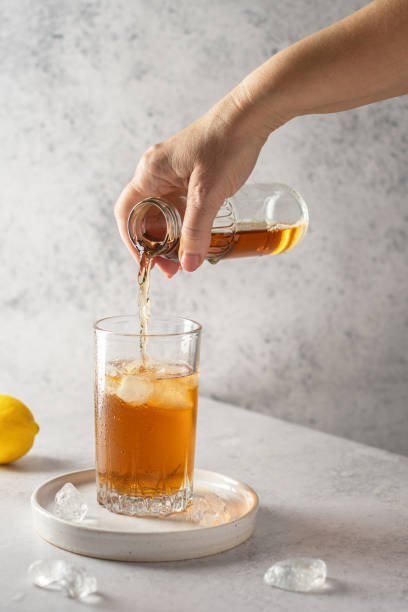 istock A woman's hand pours cold tea from a small bottle into a glass with ice. On a gray stone table are pieces of ice and a lemon. Refreshing drink in summer. 1598829372