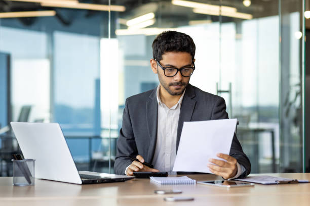 istock Serious concentrated hispanic businessman financier on paperwork inside office, man in business suit at workplace reviewing and reading papers, contracts and accounts reports. 1598829388
