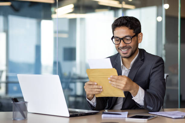 istock Young successful arab businessman at workplace inside office, man smiling satisfied received mail letter envelope notification message with good news, boss in business suit 1598829934