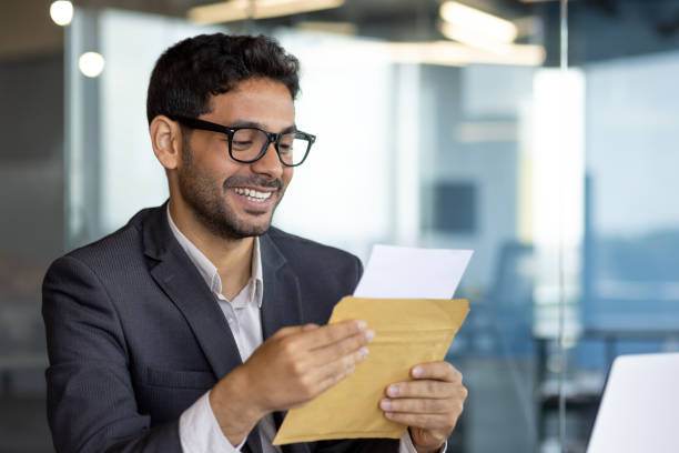 istock Young successful arab businessman at workplace inside office, man smiling satisfied received mail letter envelope notification message with good news, boss in business suit 1598829937