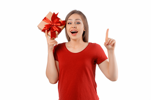 Portrait of a happy smiling girl in red t shirt holding present box and posing over white background. Cheerful brunette woman with long hair smiles, laughs and looks with joy