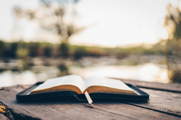 istock Open Bible on a wooden board near the river 1598837682