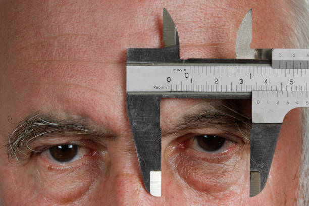 A man holds a caliper in front of his left eye and looks between the measuring jaws.
