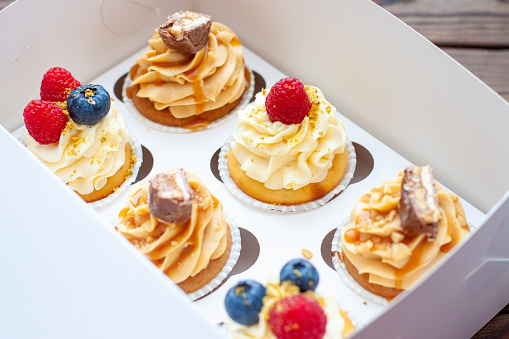 Assorted cupcakes in gift box with fresh strawberries, peanut butter, slated caramel, chocolate, raspberry, strawberry and blueberry