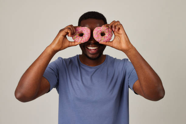 istock Smiling black man holding donuts with pink icing against his eyes 1598853134
