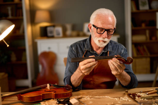 falegname senior artigiano che intaglia il legno e costruisce strumenti di violino - workshop old fashioned old instrument maker foto e immagini stock