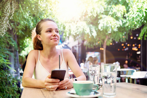 Young brunette woman sitting at the table in street cafe in summer day and waiting for the waiter.
