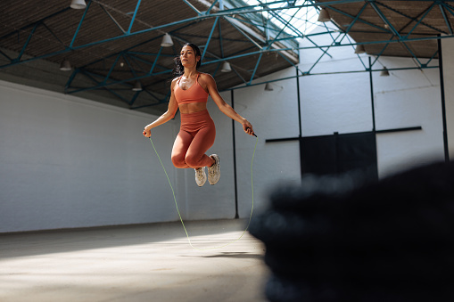 Focused woman uses her athletic technique while performing rope jumping at the fitness hangar