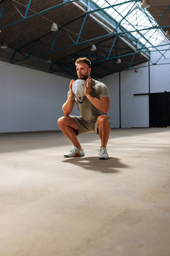 Fit man squatting while lifting a weight with his both hands at the gym