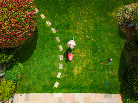 Topdown aerial view, taken by drone, depicting a man using his lawnmower to cut the grass in his back garden at home.