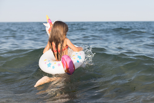 Happy baby girl swimming on an inflatable swimming unicorn in the sea.