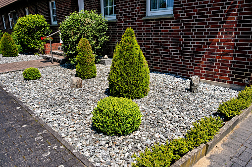 Beautiful decorative landscape design of shrubs and stones near a residential brick house in Germany.