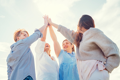 Portrait of four cheerful laughing women holding hands Up making High Five during outdoor walking. They looking at the camera. Woman's friendship, natural diversre beauty, relations, happiness image