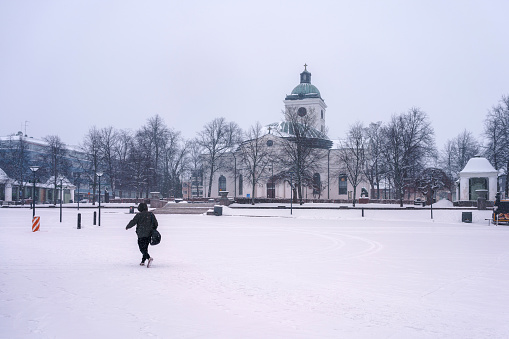 One person walking in Market Square in front of Hameenlinna church in winter. Finland, February 23, 2023.