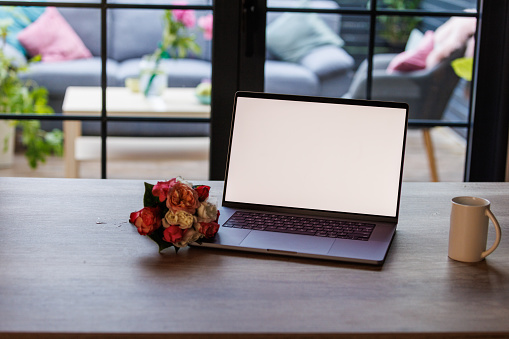 Close up shot of a laptop with a blank screen and a bouquet of roses on a table.