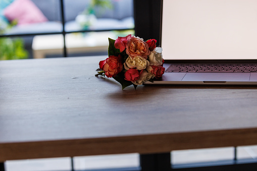 Close up shot of a laptop with a blank screen and a bouquet of roses on a table.