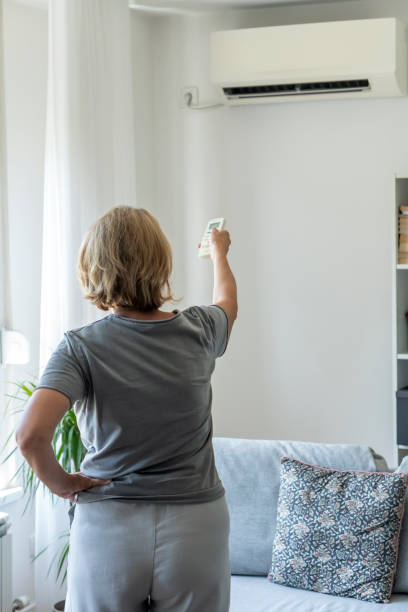 Senior woman using air conditioner at home stock photo