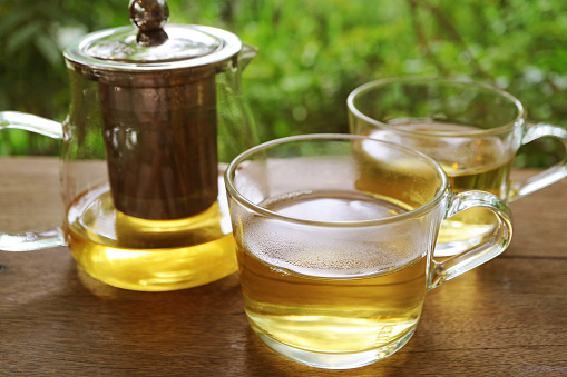 Closeup of glasses of hot tea with a tea kettle on wooden table