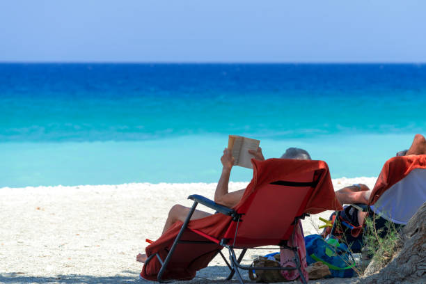 istock Man reading a book while sitting on a sun lounger on the beach. 1598998930