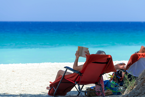 Man reading a book while sitting on a sun lounger on the beach. Rhodes, Greece