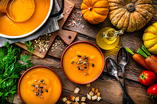Two bowls of pumpkin soup for Thanksgiving meal with ingredients on rustic wooden table