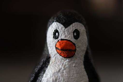 Closeup head shot of A baby Penguin made with paper mache with dark bokeh