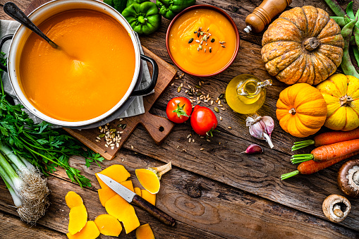 Pumpkin soup for Thanksgiving meal with ingredients on rustic wooden table