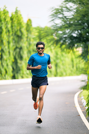 Attractive young healthy male runner is training for his long run on concrete road at park in morning. Concept of healthy lifestyle and sports
