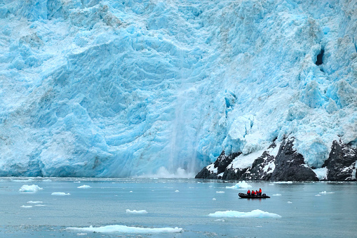 Close up view of the Aialik Glacier calving with indistinguishable figures in boat demonstrate immensity of the glacier.