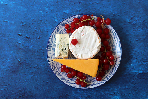 Still life with different types of cheese. Cheddar, brie, blue cheese and red currant berries on textured background with copy space.