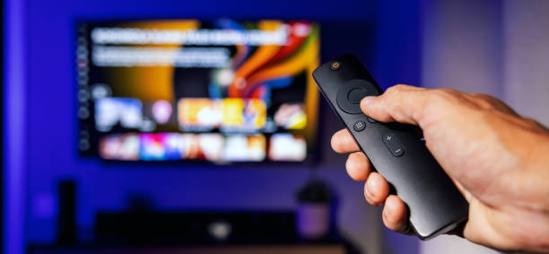 remote control in hand with tv in background at home. streaming service, content on demand. banner with copy space stock photo