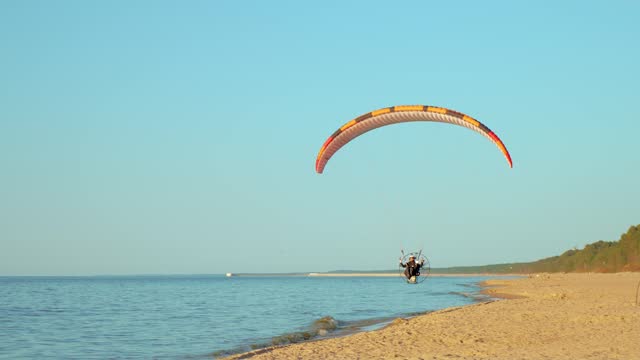 Man flying extreme paraglider with motor above sea beach