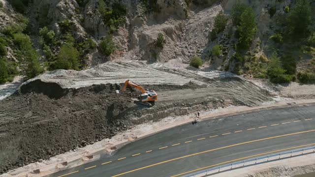 Excavator on a road construction site moving rocks, aerial view