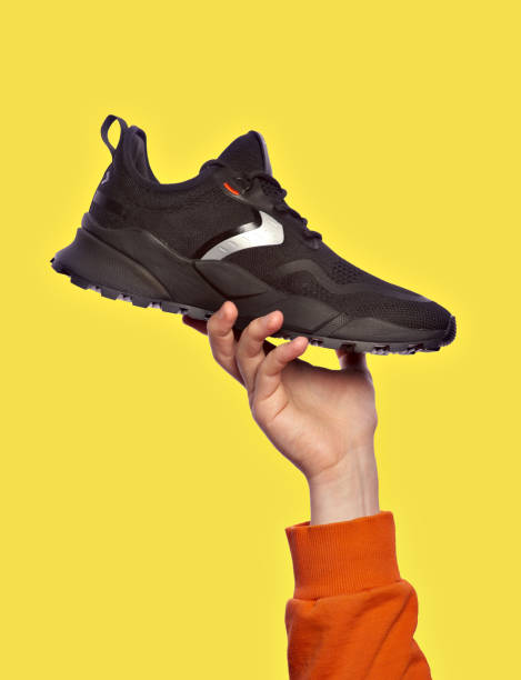 istock Stylish black sneaker presentation in a man's hand, isolated on a yellow background. Selling modern sports shoes. Advertising concept 1599096146