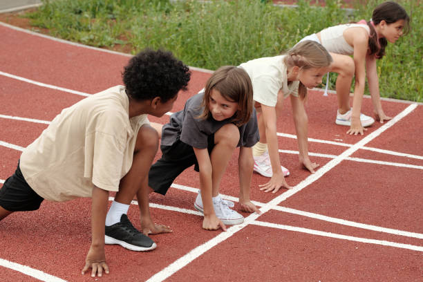 Two friendly intercultural boys looking at each other while standing by start line on stadium against schoolgirls and discussing something
