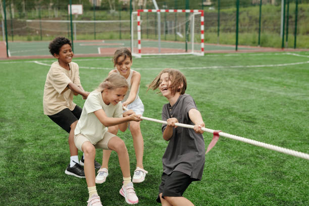 istock Cheerful schoolkids in activewear laughing while pulling rope at stadium 1599098907