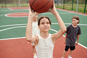 Cute schoolgirl in activewear throwing ball into basket at stadium