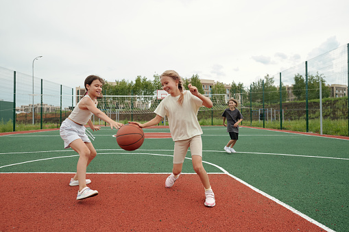 Teenagers playing basketball game together on the playground during sunny summer day