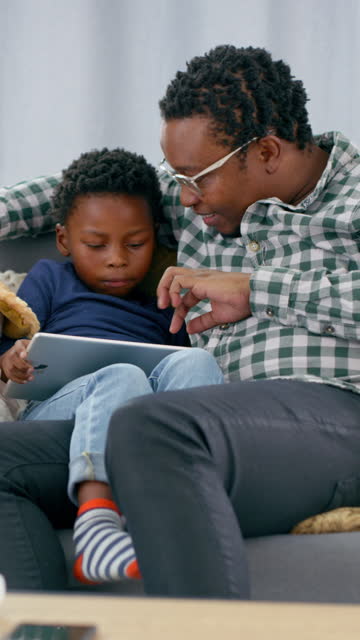 Father, boy and child with tablet in living room for online games, reading ebook story and educational media. Black man, dad and kid streaming cartoon, movies and digital technology on sofa at home