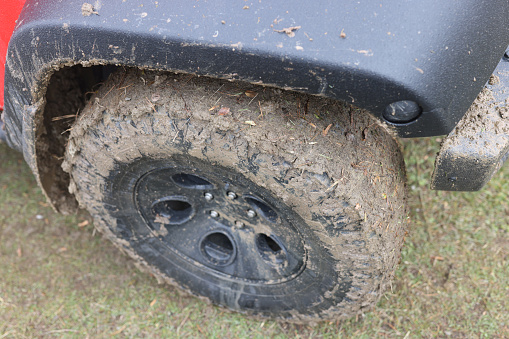 Red car wheel with dirty wheels standing on rural road closeup. Off-road driving concept