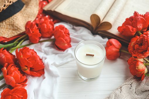 Candle, tulips and open book in home interior.