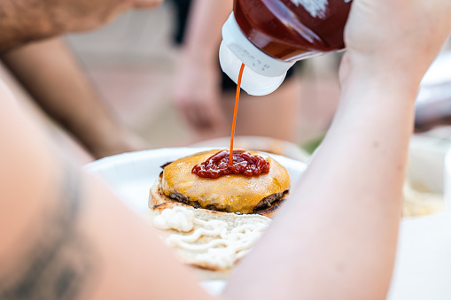 A close up shot of a person squirting ketchup onto a cheeseburger.