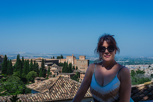 young woman looks at the camera, with the background of the nazari palaces of granada, Spain.